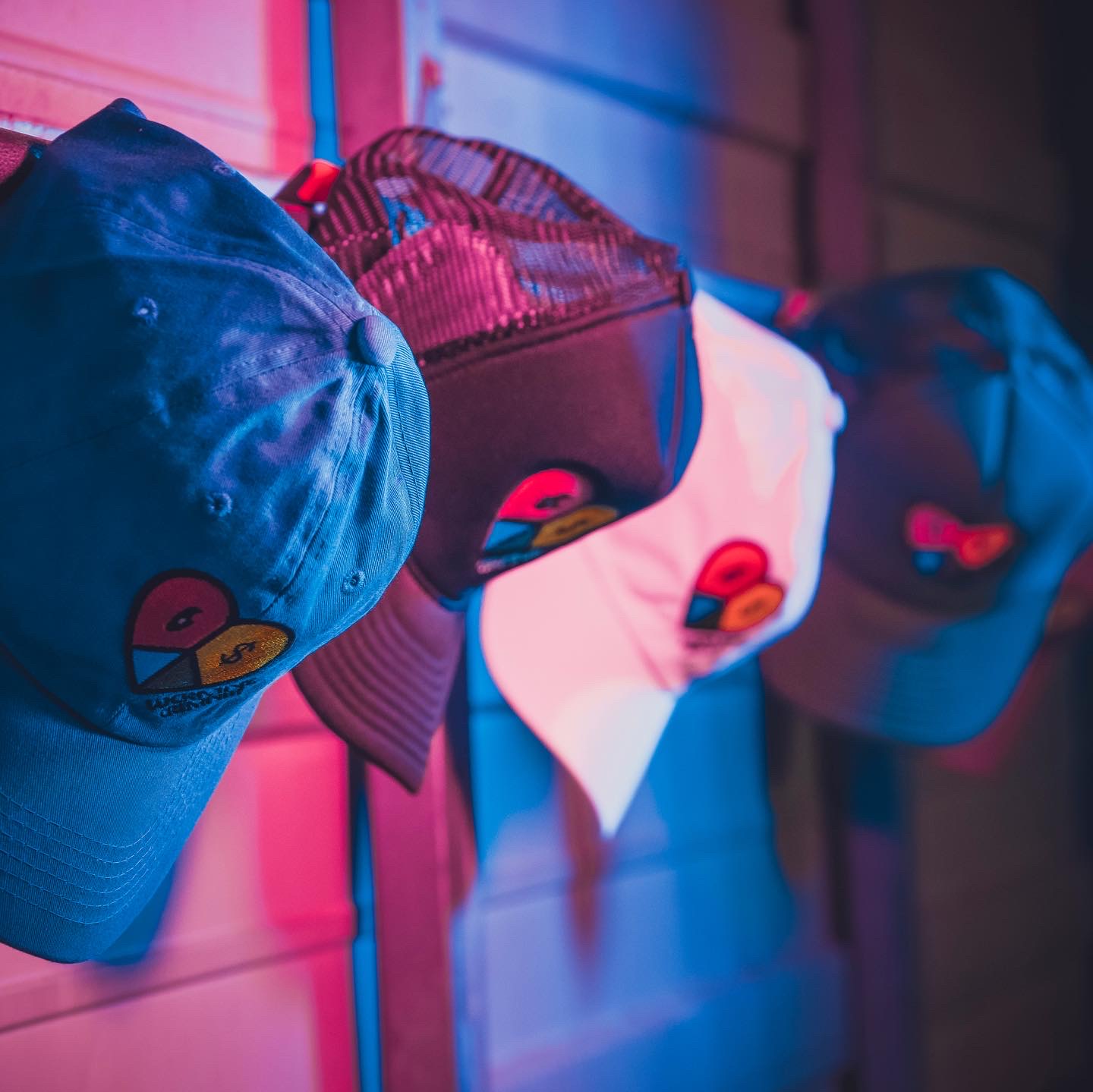 Collection of Lucrative Creativity heart-logo caps under colored studio lighting