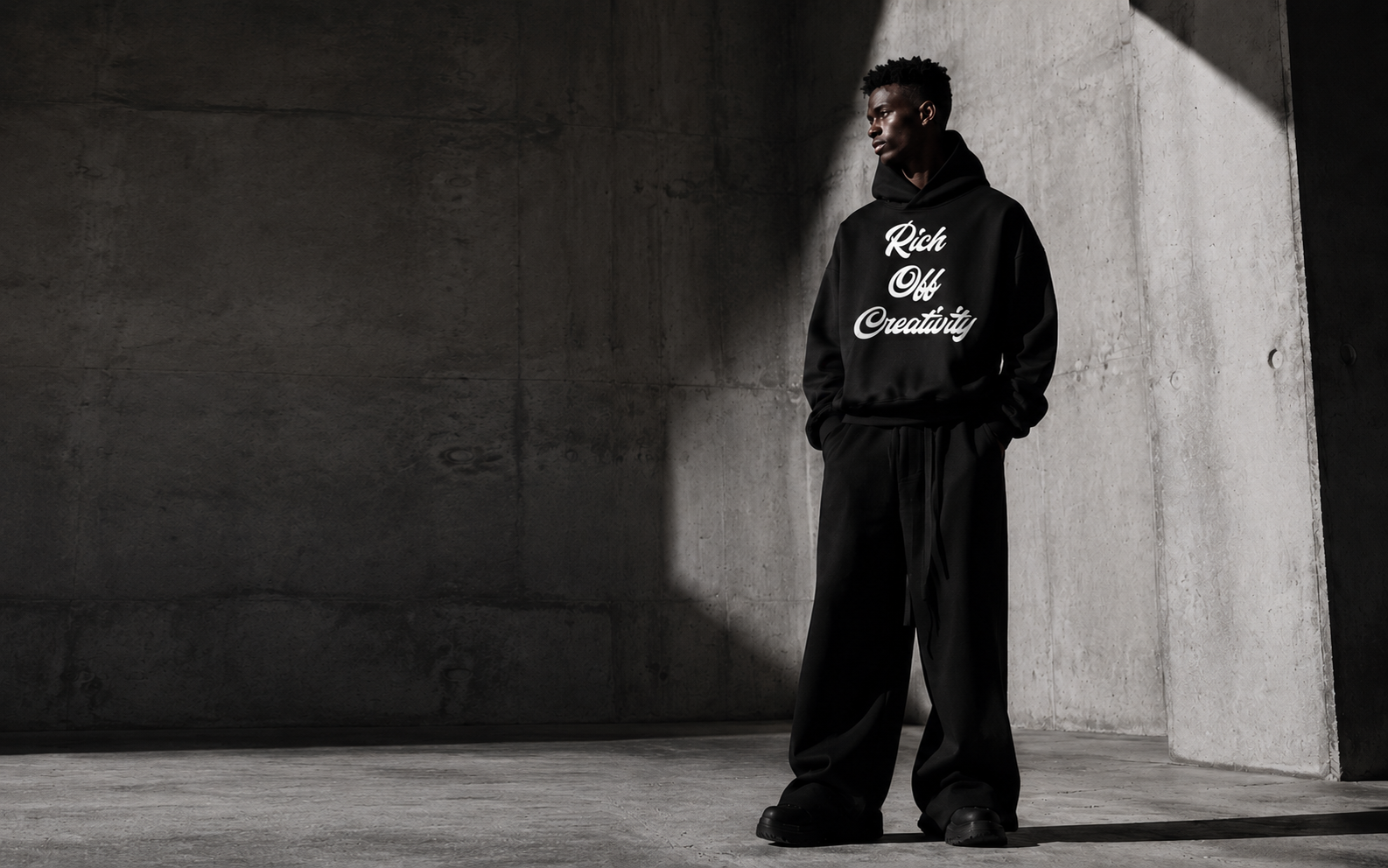 Model wearing a black Rich Off Creativity hoodie in a concrete studio