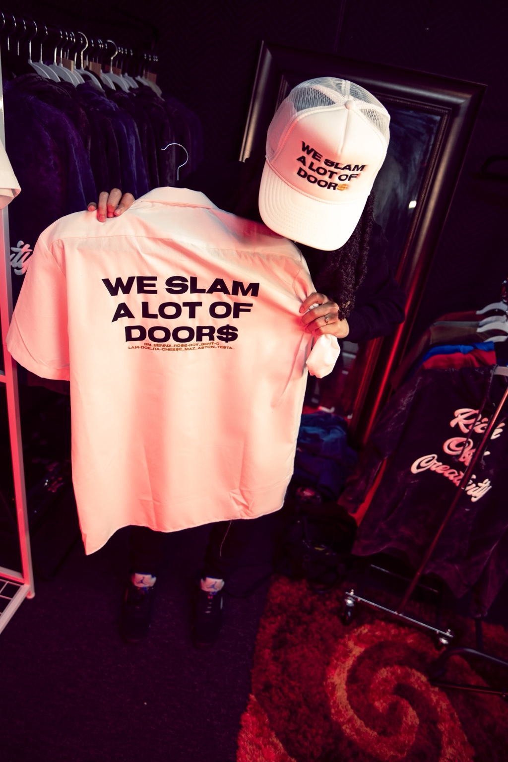 Woman holding a We Slam a Lot of Door$ shirt and cap inside the Lu.C. retail space