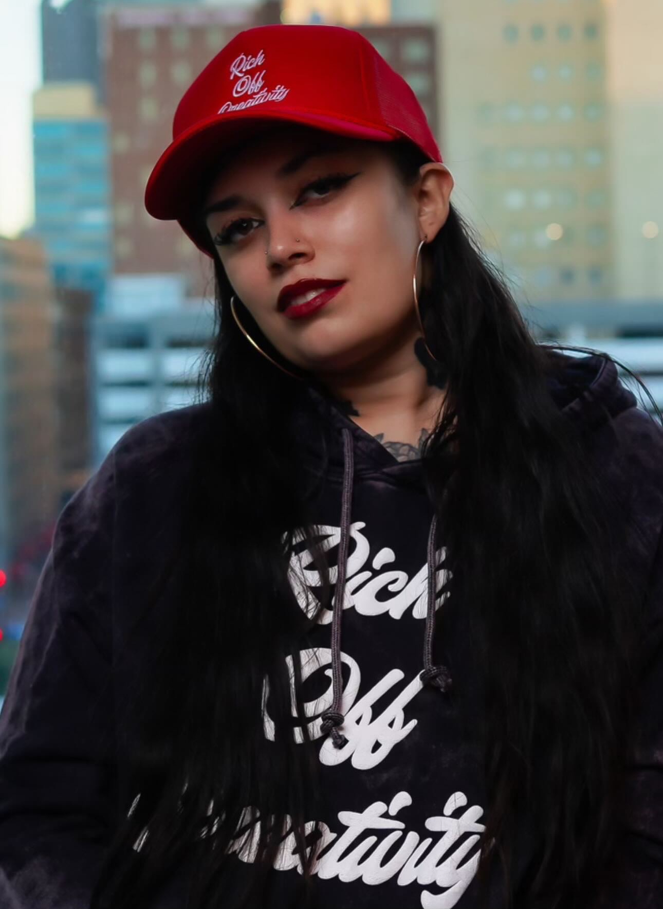 Woman wearing a Rich Off Creativity hoodie and red cap in the city